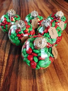 three glass christmas ornaments with candy in them on a wooden table next to a bottle of wine