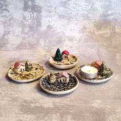 four ceramic dishes with small houses on them and candles in the middle one has a candle holder