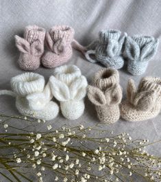 six knitted baby booties are lined up on a gray blanket next to flowers