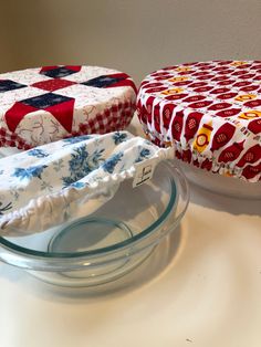 two cakes sitting on top of a table next to each other in glass bowls and covered with fabric