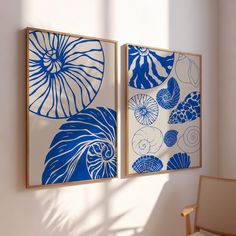 two blue and white paintings hanging on a wall next to a chair in a room