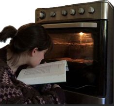 a woman reading a book in front of an oven