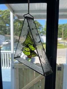 a stained glass bird feeder hanging from the side of a window with a porch in the background