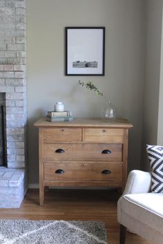 a living room with a white chair and a wooden dresser next to a fire place