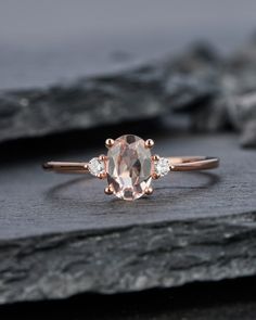 an oval cut morganite and diamond ring on top of a rock with two smaller diamonds around the band