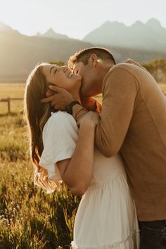 a man and woman kissing in a field with mountains in the background