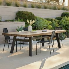 a wooden table sitting next to a pool with chairs around it and potted plants on the side