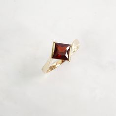 Love the way this princess cut Garnet is set in this ring! It's Gorgeous and unique.  A classic by-pass design with the sides of the gold becoming a part of the low profile design. Garnets are said to be the stone of love and friendship, and it's also January's birthstone.  (PLEASE NOTE: There's a tiny hole near one of the corners of the ring which cannot be fixed. Barely noticeable but the price has been adjusted) genuine Garnet Princess-Cut Garnet dark red color (Pyrope Garnet) measures 7 mm f Fine Jewelry Princess Cut Solitaire Birthstone Ring, Princess Cut Solitaire Birthstone Ring For Formal Occasions, Formal Square Cut Birthstone Ring In Fine Jewelry Style, Fine Jewelry Square Cut Birthstone Ring For Formal Occasions, Square Cut Birthstone Ring For Formal Events, Square Cut Birthstone Ring For Formal Occasions, Formal Square Cut Birthstone Ring, Gold Ruby Ring With Tension Setting For Formal Occasions, Classic Princess Cut Ruby Ring As Gift