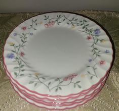 three pink and white plates with flowers on them sitting on a lace covered tablecloth