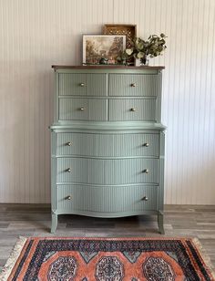 a green dresser sitting on top of a wooden floor next to a painting and rug