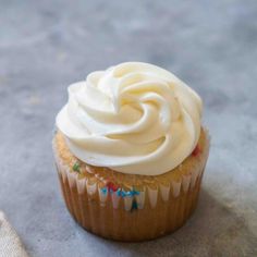 a cupcake with white frosting sitting on top of a table next to a napkin