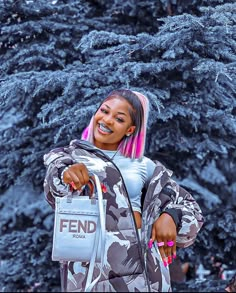 a woman with pink hair holding onto a handbag in front of a pine tree