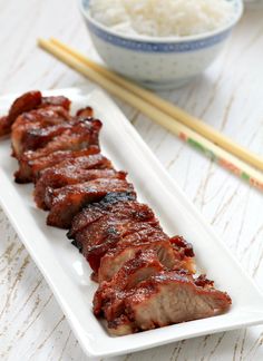 a white plate topped with meat next to chopsticks