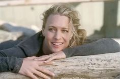 a woman leaning on a log with her arms crossed and smiling at the camera,