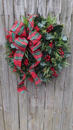 a christmas wreath with red berries and green leaves on a wooden fence, hanging from the side of a house