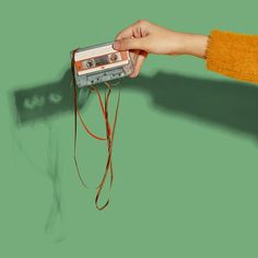 a person holding an old fashioned cassette player in their left hand, against a green background