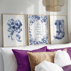 three blue and white pictures hanging on the wall above a bed with purple pillows in front of them