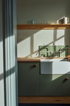 a kitchen with green and white tiles on the wall, sink and shelving unit