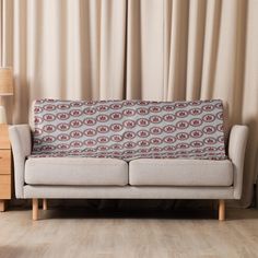 a white couch sitting in front of a window next to a wooden table with a lamp on it