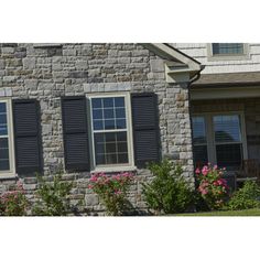 a brick house with two windows and shutters on each side, surrounded by pink flowers