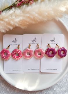 four pink donuts with sprinkles are on a white plate next to a feather