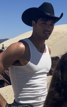 a man wearing a cowboy hat standing next to a woman in a white tank top