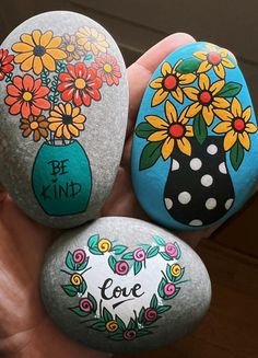 three painted rocks in the shape of vases with flowers