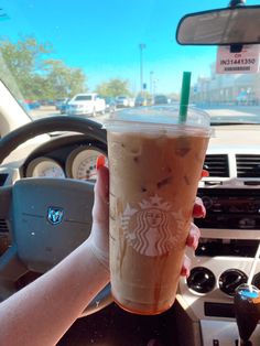 a person holding up a starbucks drink in their hand on the steering wheel of a car