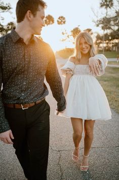 a man and woman are walking down the street holding hands as the sun sets behind them