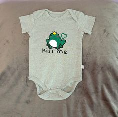 "Your little one can be styling while wearing this cute \"Kiss Me\"  bodysuit with adorable frog graphic. Items are finished and ready to ship. Most items are shipped next day but may take up to 3 days to ship. Design is made of premium Heat Transfer Vinyl using a heat press to ensure a quality bond. HONEST® Baby Clothing bodysuit is made from 100% Organic Cotton. Care: Wash cold, inside out, gentle cycle. Mild detergent, Non-chlorine bleach when needed. Tumble dry low. Iron inside out only if needed. Do not dry clean. HONEST® Baby Clothing bodysuit run close to size so be sure to check size chart below for fit. HONEST® SIZES  0-3 Months :: 21-24 in. / 10-14 Ibs. 3-6 Months :: 24-27 in. / 15-18 Ibs.  6-9 Months :: 27-29 in. / 19-22 Ibs. 12 Months :: 29-31 in. / 23-25 Ibs. 18 Months :: 31-3 Frog Graphic, Honest Baby Products, Cute Kiss, Ship Design, Low Iron, Gender Neutral Baby, Transfer Vinyl, Baby Clothing, Kiss Me