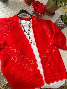 a red knitted sweater with white trim sits on a table next to some flowers