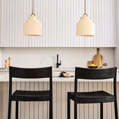 two black chairs sitting next to each other in front of a kitchen counter with lights on