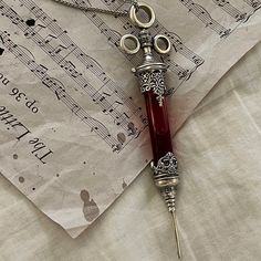 a red glass pen sitting on top of sheet music paper next to a pair of scissors