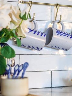 two mugs are hanging on the wall next to flowers