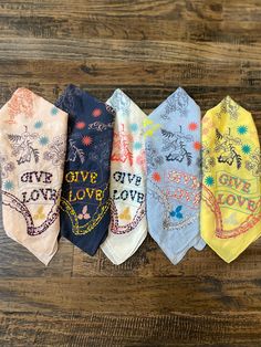 five ties with different designs on them sitting on a wooden surface, one has the words give love written on it