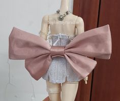 a mannequin with a pink bow on it's head is standing next to a wall