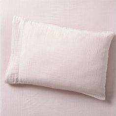 a white pillow sitting on top of a bed next to a pink sheeted wall