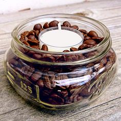 a glass jar filled with coffee beans sitting on top of a wooden table next to a white candle