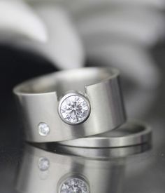 two silver rings with diamonds on them sitting on top of a table next to each other