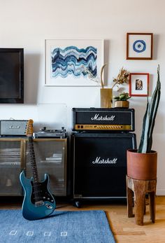 an electric guitar and amps sit on a rug in front of a wall with pictures