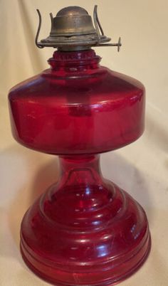 an old fashioned red glass lamp with a bell on it's top, sitting on a white surface