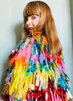 a woman with long red hair wearing a multicolored fringed dress and smiling