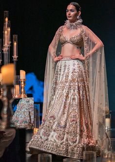 This enchanting earthy beige lehenga set is a beautiful blend of exuberance and grandeur. An ensemble that you will want this wedding season includes a lehenga, a blouse, a dupatta and a veil. Stitched to perfection, the lehenga features 3D embroideries with organza flowers using pearls, salli, cutdana, and stud tassels. The sleeveless blouse features a scintillating sweetheart neckline with handcrafted finish and a back hook closure. Paired with a heavy net dupatta, the cut-work detailing and intricate embroidery take center-stage. The lehenga comes with an attached cancan and the blouse has padding. Completed with a veil, this opulent ensemble silhouette will glimmer in the spotlight. Dry-clean only if required. Slight variation in color is possible due to digital photography. Festive Floor-length Gown For Wedding Reception, Festive Resham Embroidered Lehenga For Wedding Reception, Festive Resham Embroidery Lehenga For Wedding Reception, Anarkali Floor-length Gown For Wedding Reception, Festive Lehenga With Dupatta For Wedding Reception, Bollywood Style Dresses For Wedding Reception, Floor-length Lehenga With Intricate Embroidery For Wedding Reception, Elegant Lehenga With Intricate Embroidery For Wedding Reception, Elegant Lehenga With Dupatta For Wedding Reception