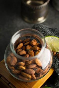 nuts and limes are in a glass jar on a wooden tray next to a towel