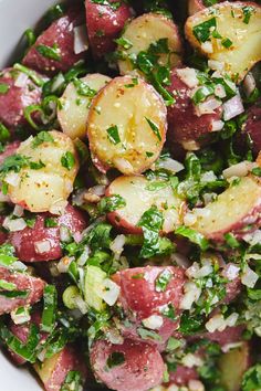 a white bowl filled with potatoes, onions and green herbs on top of a wooden table