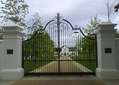 an iron gate with two pillars leading into a driveway