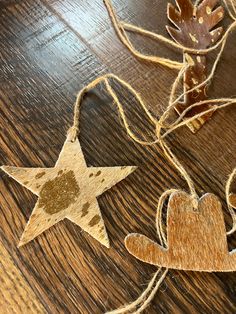 two wooden stars are hanging from twine on a wood table, one is brown and the other is gold