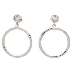 A stylish pair of contemporary diamond circle drop earrings set in 14k white gold. Each earring features a rub over set round brilliant cut diamond which is secured with a post and butterfly fitting. Hanging freely from this stud is a solid openwork white gold circle. Due to the design and size these earrings could be worn for a variety of occasions. There is a combined diamond weight of approximately 0.40 carats. These diamonds are G-H in colour with VS-SI clarity. For size reference the circle Minimalist Round Diamond Earrings For Formal Occasions, Modern White Gold Earrings With Bezel Setting, Modern Diamond Earrings With Bezel Setting, Modern Round Cut Halo Diamond Earrings, Modern White Gold Hoop Earrings With Single Diamond, Silver Diamond Hoop Earrings With Single Diamond, Modern Round Diamond Earrings As Gift, Formal Round Diamond Earrings With Polished Finish, Modern Diamond Earrings With Halo Design