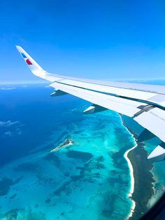 an airplane wing flying over the ocean and coral reef area in the foreground, taken from above