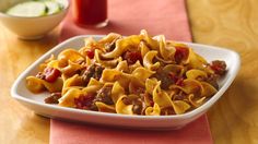 a white plate filled with pasta and meat on top of a wooden table next to a bowl of broccoli